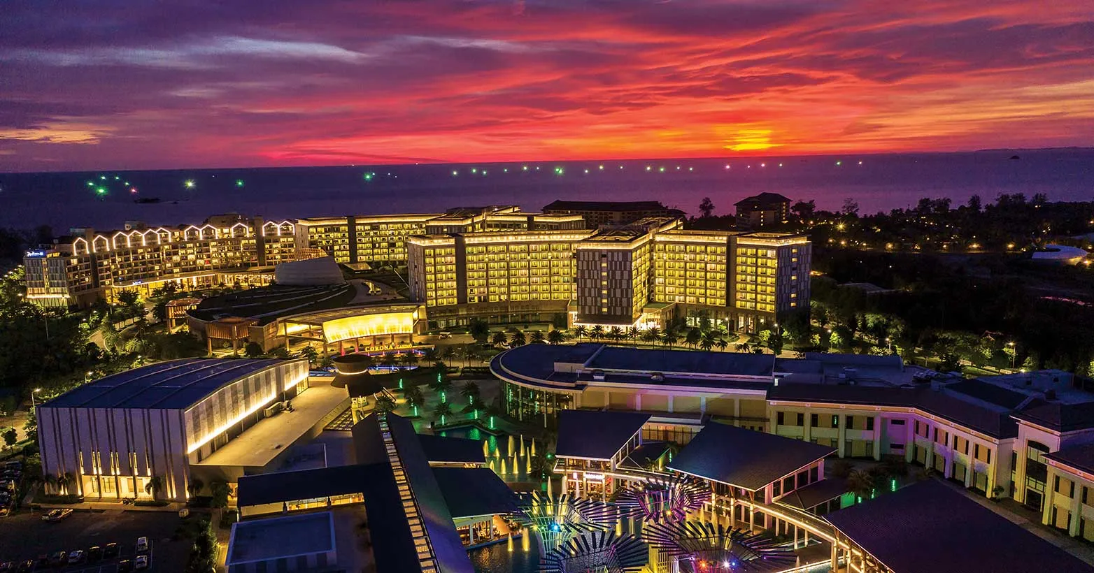 Aerial view at sunset of the Bai Dai resort complex lit up, with the Corona Casino signage visible on the central building