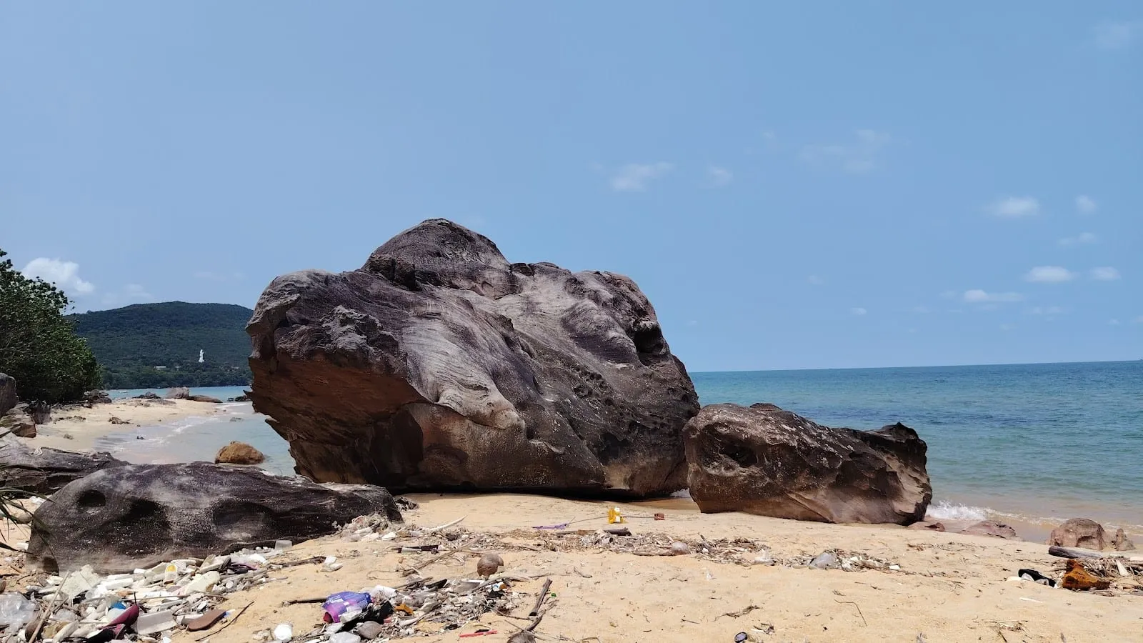 Large dark boulders on the sand at Bai Dam, with the sea and a headland behind
