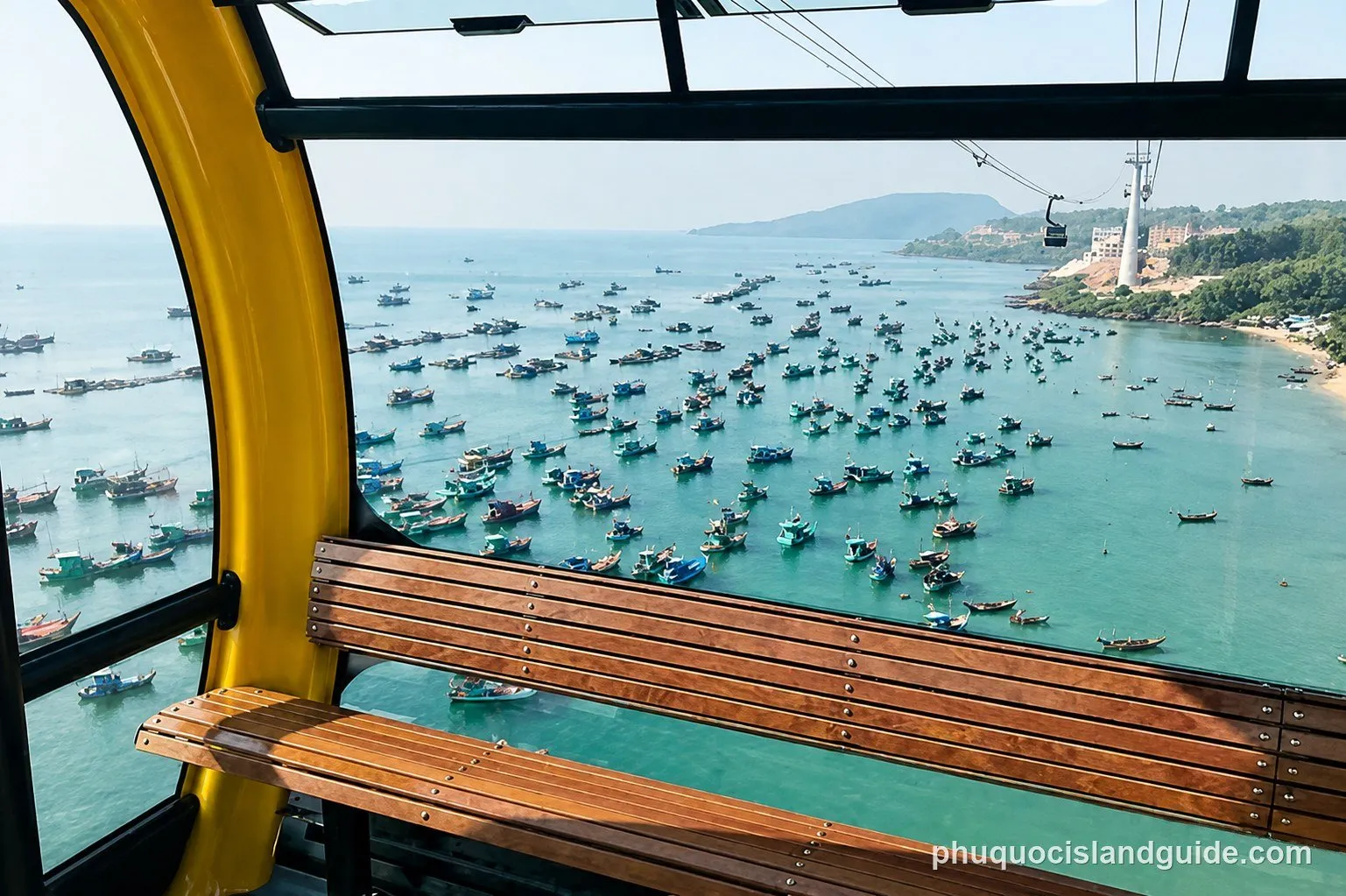 A view from inside a cable car cabin looking out over a bay filled with numerous fishing boats, with a coastline and hills in the distance.