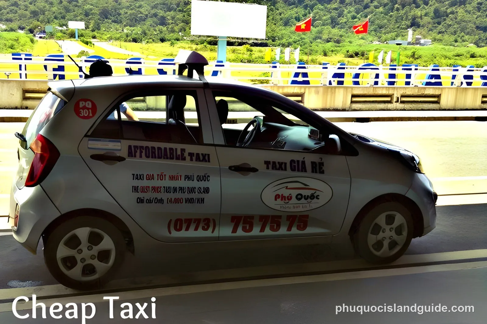 A silver taxi car with ‘Affordable Taxi’ and ‘Phu Quoc’ branding on its side, parked on a road. Green hills and Vietnamese flags are visible in the background.