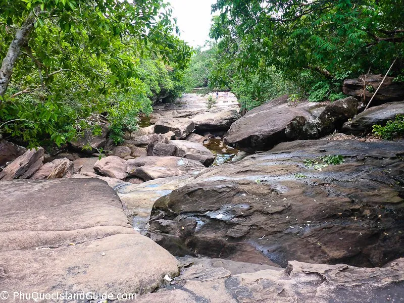 Broad granite boulders and shallow pools of the Suoi Da Ban stream bed, enclosed by jungle